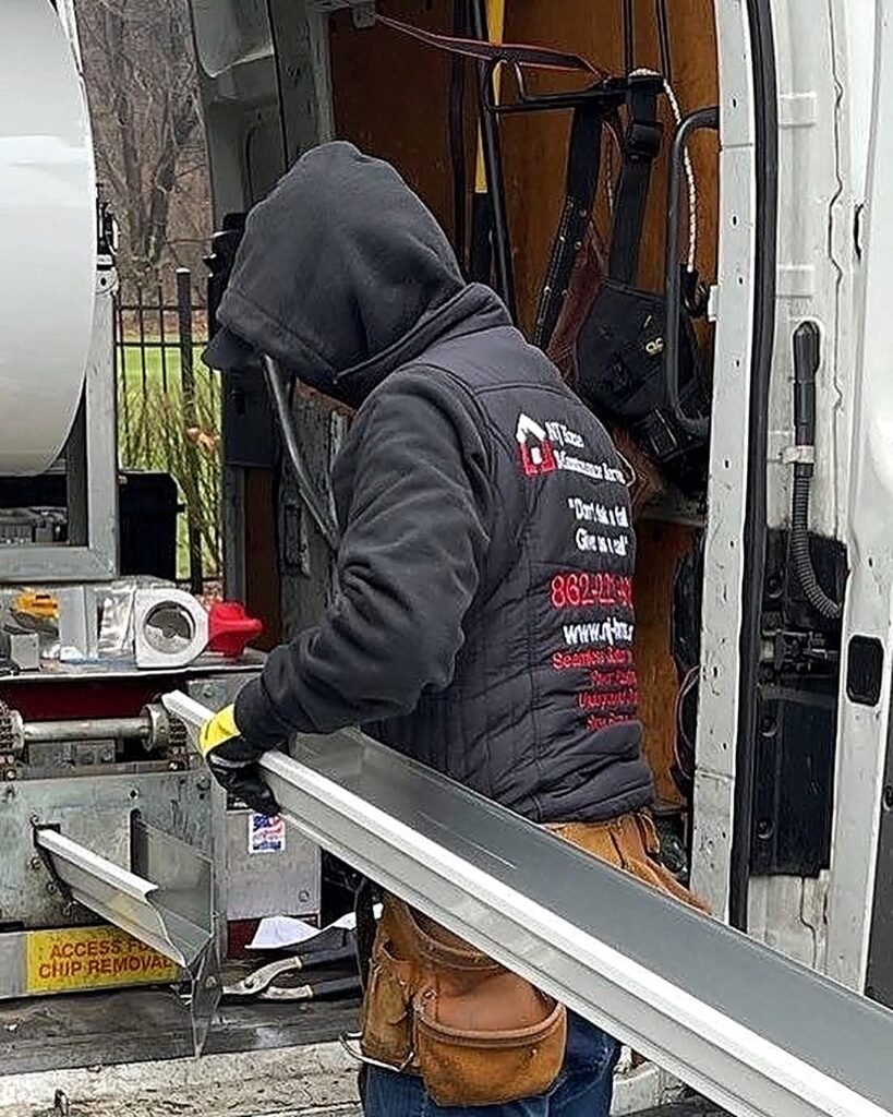NJHMS technician feeding aluminum coil through a seamless gutter machine at the back of the install truck