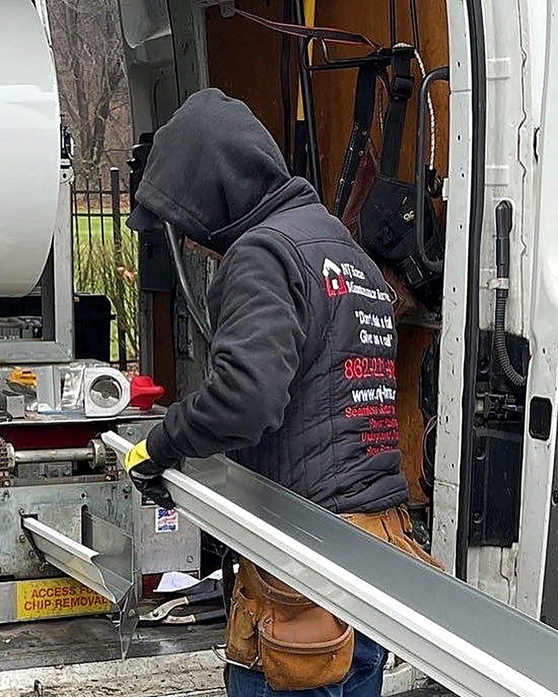 NJHMS technician feeding aluminum coil through a seamless gutter machine at the back of the install truck