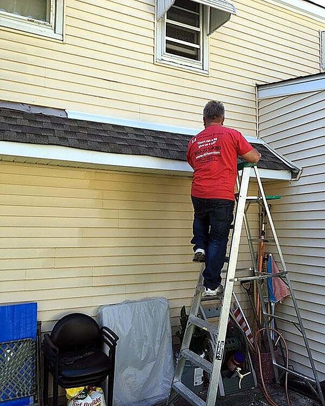 NJHMS technician on a ladder working on fascia and gutter trim along a roofline