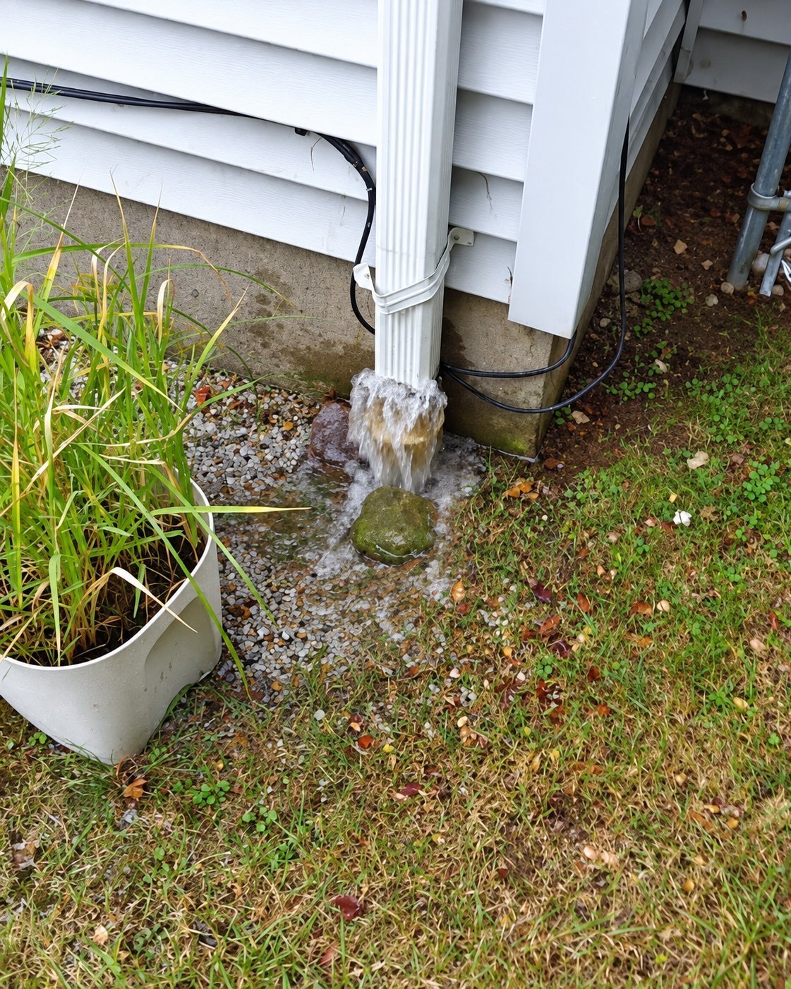Downspout releasing water onto the ground right next to a house foundation