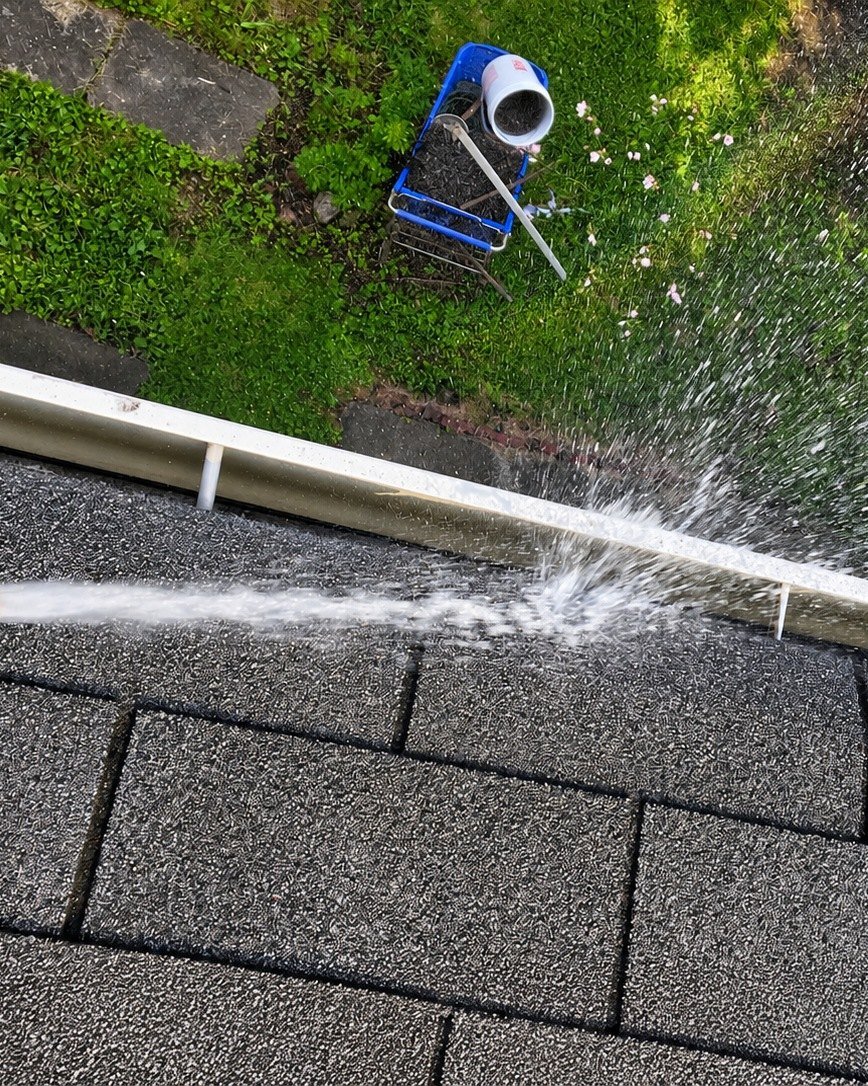 Hose nozzle flushing water along a gutter on the roof edge